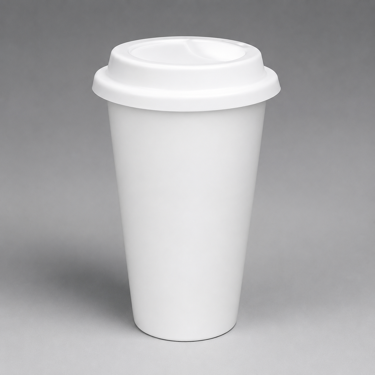 A plain white reusable travel cup with a matching white lid, photographed on a smooth gray studio background.